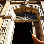 A conservation architect meticulously examining the facade of an old Portuguese building, using tools to assess the stone and mortar, with sunlight highlighting the intricate details and signs of weathering. Emphasize the balance between preservation and functionality.